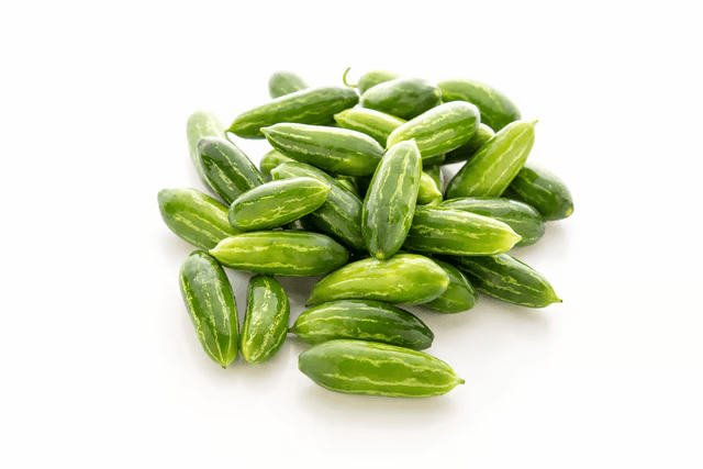 Pile of small, green striped cucumbers on a white background, fresh and ready to eat. - Tindora