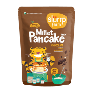 Brown pouch of Slurrp Farm Millet Pancake mix, chocolate flavor, featuring a smiling tiger serving pancakes with a bowl of batter nearby on the package. - Slurrp Farm Millet Pancake Mix Chocolate 150g
