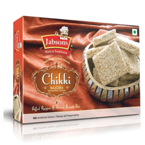 Box of Jabsons Chikki Rajgira traditional Indian sweets with sesame and peanuts, shown with pieces in a bowl on the packaging side. - Jabsons Chikki Rajgira 130gm